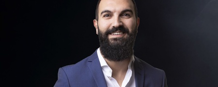 Man i blå kostym står bredvid en amerikansk flagga mot mörk bakgrund.