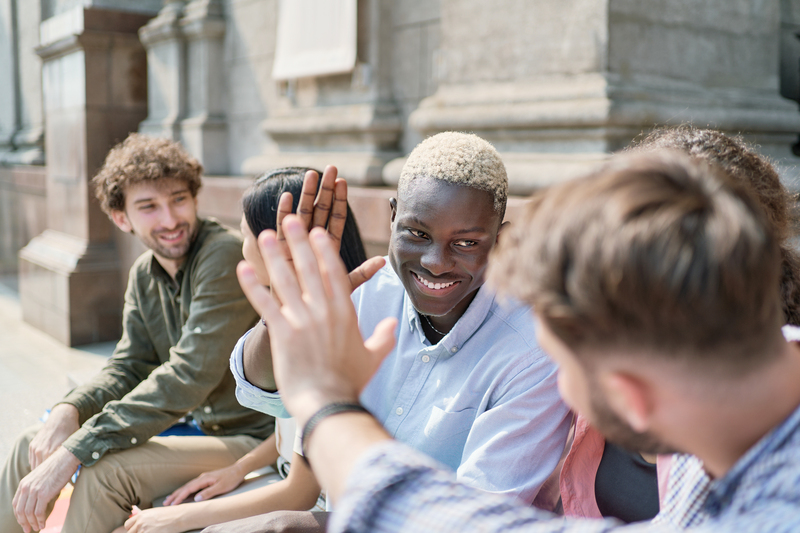 En grupp unga vuxna sitter utomhus och två personer ger varandra en high five.